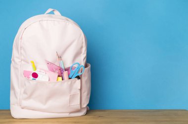 Ahşap masada kırtasiye malzemesi olan pembe okul çantası.