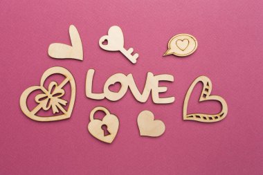 Wooden word love with hearts on color background, top view