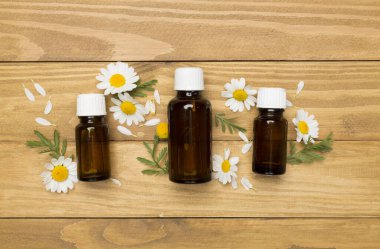 Papatya çayı şişeleri ve ahşap arka planda çiçekler, üst manzara.