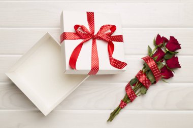 Open gift box with red roses on wooden background, top view