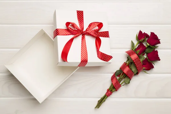 Open gift box with red roses on wooden background, top view