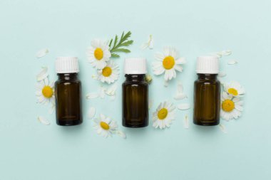 İçinde papatya çayı bulunan şişeler esaslı yağ ve renk arka planında çiçekler, üst görünüm