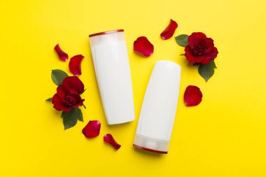 Hair care products and red roses on color background, top view