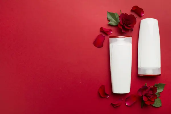 Hair care products and red roses on color background, top view