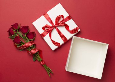 Open gift box with red roses on color background, top view