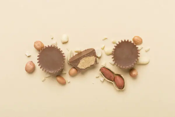 Tasty chocolate peanut butter cups with nuts on color background, top view