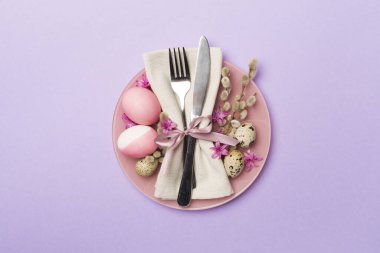 Arka planda bahar çiçekleri ve çatal bıçak seti olan Paskalya masası, üst görünüm