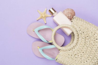 Çocuksu parmak arası terliklerle dolu plaj çantası ve arka planda güneş koruması, üst manzara.