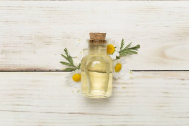 Şişe papatya çayı esaslı yağ ve ahşap arka planda çiçekler, üst manzara.