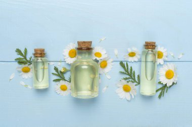 Papatya çayı şişeleri ve ahşap arka planda çiçekler, üst manzara.