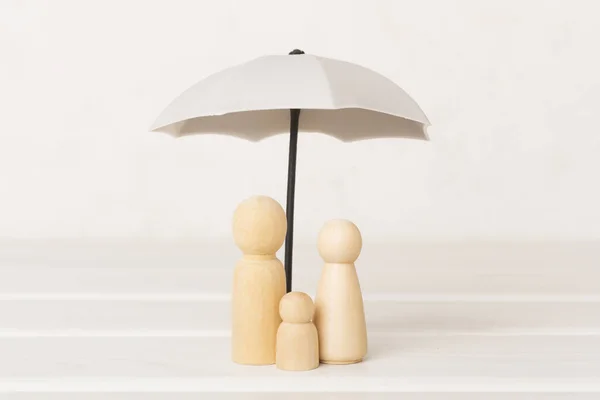 Wooden family figures under umbrella on wooden table