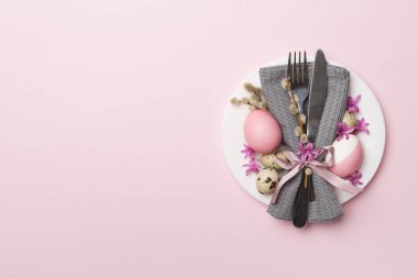 Arka planda bahar çiçekleri ve çatal bıçak seti olan Paskalya masası, üst görünüm