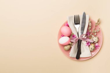 Arka planda bahar çiçekleri ve çatal bıçak seti olan Paskalya masası, üst görünüm