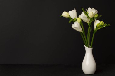 Masanın üzerinde vazoda duran beyaz frezya çiçekleri.
