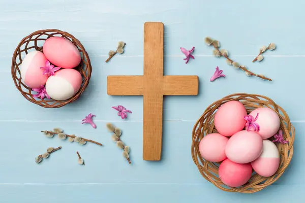 Pink Easter eggs with cross and leaves on wooden background, top view