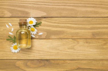 Şişe papatya çayı esaslı yağ ve ahşap arka planda çiçekler, üst manzara.