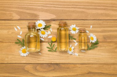 Papatya çayı şişeleri ve ahşap arka planda çiçekler, üst manzara.