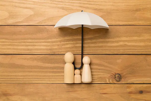 Umbrella and wooden family figures on wooden background, top view. Insurance coverage concept.