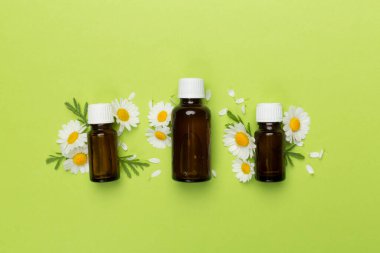 İçinde papatya çayı bulunan şişeler esaslı yağ ve renk arka planında çiçekler, üst görünüm