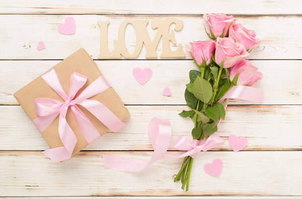 Pink roses with hearts and gift box on wooden background, top view.