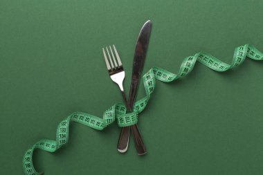 Renk arkaplanı ve üst görünümde mezuraya sarılı bıçak ve çatal