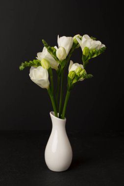 Masanın üzerinde vazoda duran beyaz frezya çiçekleri.