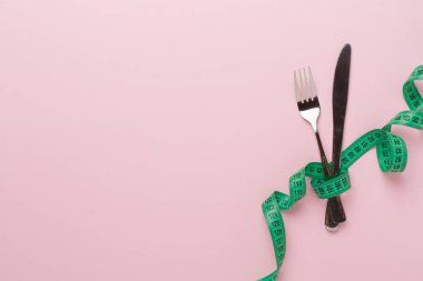 Renk arkaplanı ve üst görünümde mezuraya sarılı bıçak ve çatal