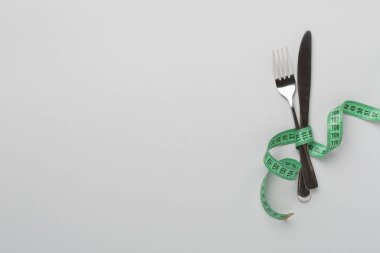 Renk arkaplanı ve üst görünümde mezuraya sarılı bıçak ve çatal