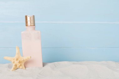 Kum üzerinde yaz dekoru olan güneş kremi ahşap arka planda