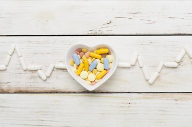 Kardiyogram, ilaçlarla ve tahta arka planda kalp şeklindeki kaseyle yapılmış.