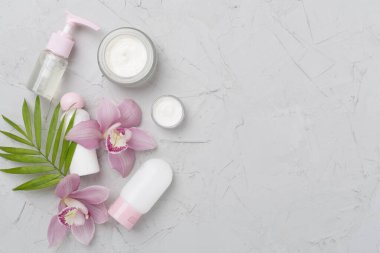 Beton arka planda kremalı ve orkideli şişeler ve kavanozlar.