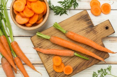 Tahta arka planda dilimlenmiş havuçlarla dolu taze havuçlar.