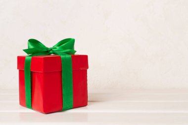 Yeşil kurdeleli kırmızı hediye kutusu ve masanın üstünde fiyonk