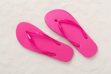 Kum arka planında parlak parmak arası terlikler, üst manzara. Yaz konsepti