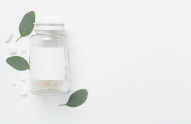 İlaç şişesi ve beyaz arka planda yeşil yapraklar, üst görünüm