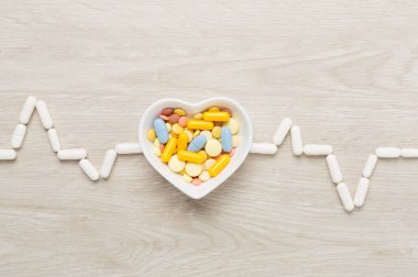 Kardiyogram, ilaçlarla ve tahta arka planda kalp şeklindeki kaseyle yapılmış.