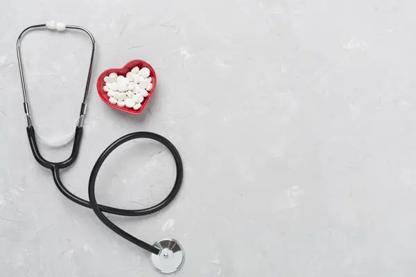 stock image Stethoscope with heart medicines on concrete background, top view