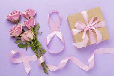 Pembe güllü kompozisyon, hediye kutusu ve arka planda sekizli kurdele, üst manzara. Kadınlar Günü konsepti