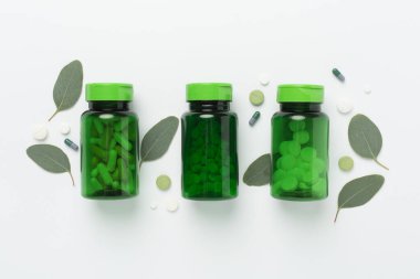 İlaç şişesi ve beyaz arka planda yeşil yapraklar, üst görünüm