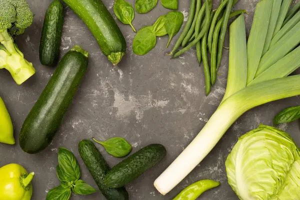 Beton arka planda farklı yeşil sebzeler, üst manzara.