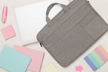 Beton zemin üzerinde kırtasiye malzemesi olan gri renkli laptop çantası, üst görünüm.