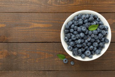 Ahşap arka planda taze yaban mersinli kase, üst manzara.