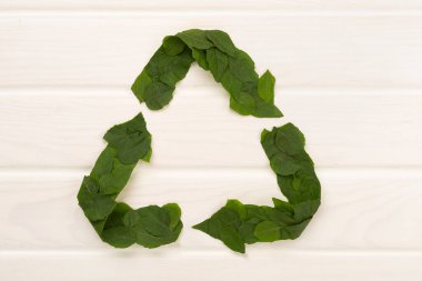 Ahşap arka planda yeşil yapraklardan yapılmış geri dönüşüm sembolü, üst görünüm