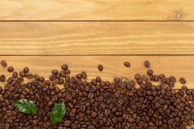 Ahşap arka planda yaprakları olan kavrulmuş kahve çekirdekleri.