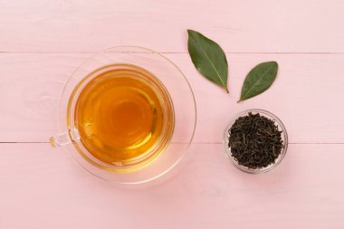 Tahta arka planda kuru ve taze yapraklı bir fincan çay, üst manzara.