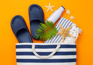 Renkli arka planda yaz aksesuarları olan mavi plaj çantası, üst manzara.