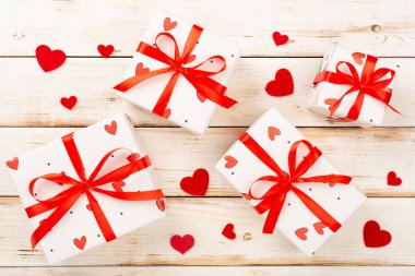 Ahşap zemin üzerinde kırmızı kalpler olan şenlikli hediye kutuları.