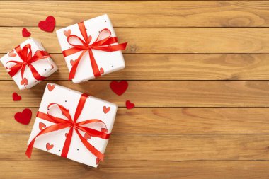 Ahşap zemin üzerinde kırmızı kalpler olan şenlikli hediye kutuları.