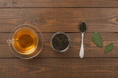 Tahta arka planda kuru ve taze yapraklı bir fincan çay, üst manzara.