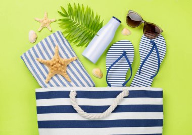 Renkli arka planda yaz aksesuarları olan mavi plaj çantası, üst manzara.